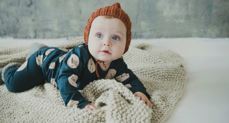 Cute baby in cozy knitted outfit lying on a soft blanket indoors.