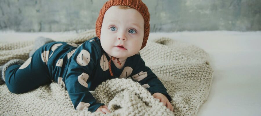 Cute baby in cozy knitted outfit lying on a soft blanket indoors.